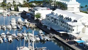 A marina with multiple boats docked, surrounded by buildings with distinct architectural styles, including a prominent white building with a unique roof design. - Charming studio overlooking Saint-François marina, golf course, lagoon & beach on foot. (Saint-François)