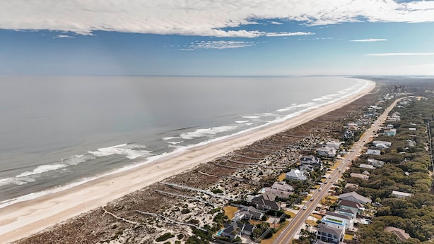 Vista aérea de una zona costera con una playa, una carretera bordeada de casas y un puente que las conecta.