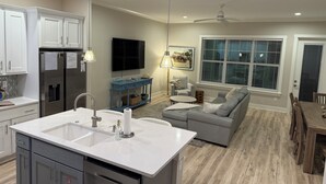 Una cocina moderna con una isla central, un comedor con mesa de madera y una sala de estar con sofá gris.