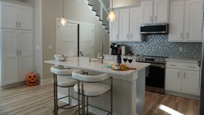 Una cocina moderna con armarios blancos, una isla central con taburetes y horno integrado, además de un microondas.