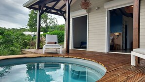Et poolområde med træterrasse, en stol og en overdækket patio.