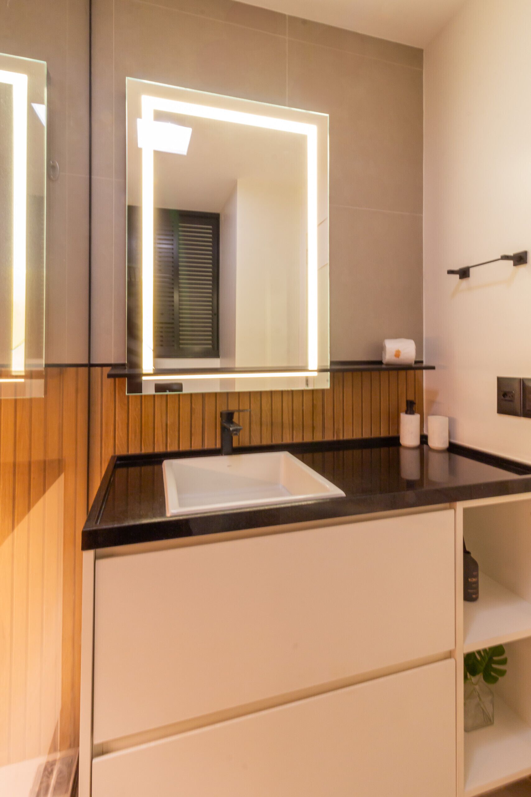 A modern bathroom with a large mirror, a white sink, and wooden paneling.