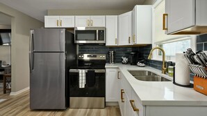 A modern kitchen with stainless steel appliances, white cabinetry, and a black tiled backsplash. - 4BR | 4 King Beds | Near Arrowhead | Pets (Blue Springs)
