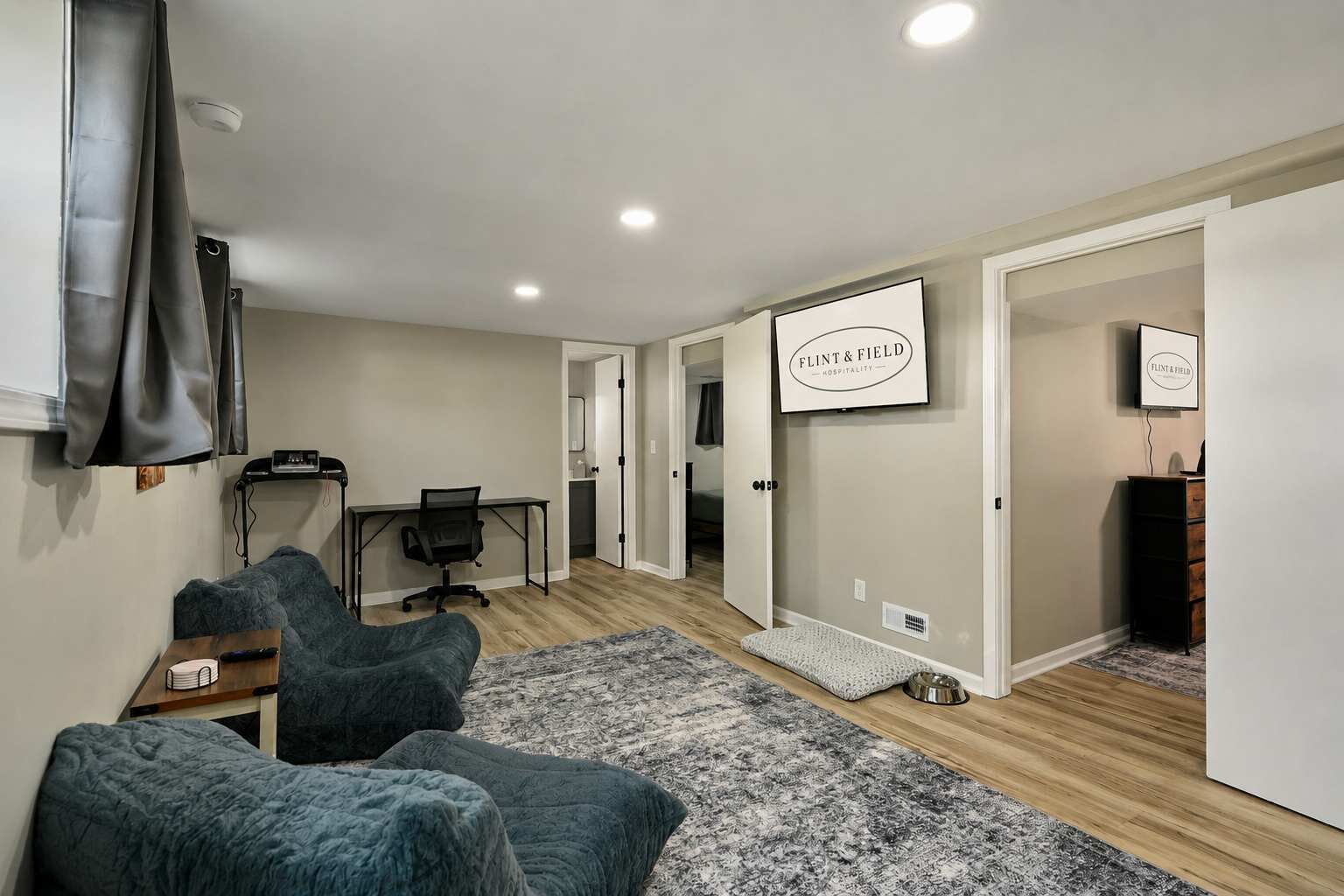 A modern living room with a sofa, a desk, and a computer. There is a sign on the wall and a television mounted on the wall.