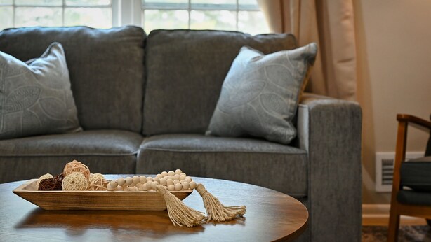 A living room with a grey sofa, a wooden coffee table, and a window with curtains. - 4BR | 4 King Beds | Near Arrowhead | Pets (Blue Springs)