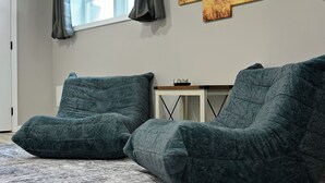 A room with two green bean bag chairs on a patterned rug, a small white side table with a black object, and a large abstract painting on the wall. - 4BR | 4 King Beds | Near Arrowhead | Pets (Blue Springs)