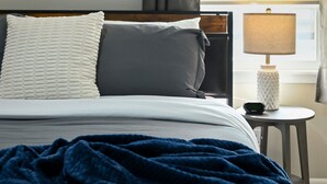 A neatly made bed with a white and gray pillow, a blue blanket, and a bedside table with a lamp and a clock. - 4BR | 4 King Beds | Near Arrowhead | Pets (Blue Springs)
