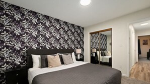 A bedroom with a large bed, a nightstand, a mirror, and a patterned wallpaper.