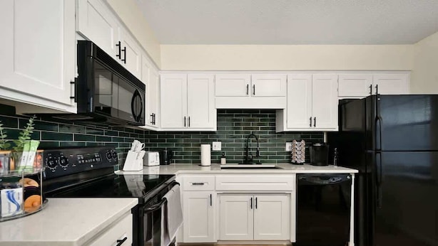 A modern kitchen with white cabinets, a black refrigerator, a microwave, and a stove.