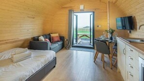 Ein gemütliches Blockhaus mit Holzvertäfelung, einem Bett, einer Couch, einem Essbereich und einem an der Wand befestigten Fernseher.