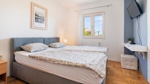 Een slaapkamer met een bed, een nachtkastje, een raam met uitzicht, een tv aan de muur en een foto in een lijst.