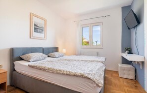 Une chambre à coucher avec un lit, une table de chevet, une fenêtre donnant sur un beau paysage, un téléviseur fixé au mur et un tableau encadré accroché au mur.