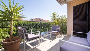 Een balkon met twee stoelen, een tafel, een bloempot en uitzicht op gebouwen.