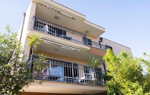 Ein mehrgeschossiges Wohngebäude mit Balkonen, einer flachen Dachterrasse und umliegender Bepflanzung.