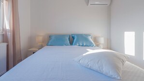 Ein Schlafzimmer mit einem Bett, zwei Nachttischlampen, einem Fenster mit Vorhängen und einer Klimaanlage.