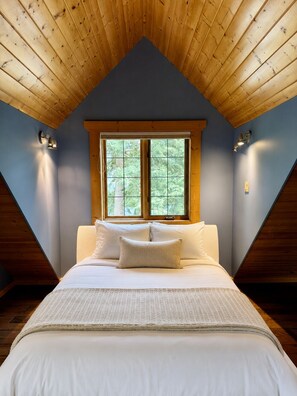 Een slaapkamer met een schuine kap, een groot raam en een bed met witte beddengoed.