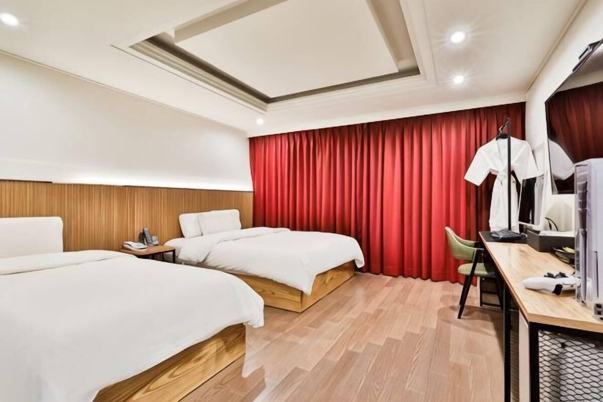 A hotel room with two beds, a desk, a chair, a wardrobe, and a red curtain.