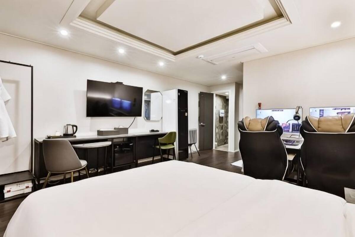 A hotel room with a large bed, a desk with a computer, a television, and a seating area with chairs.