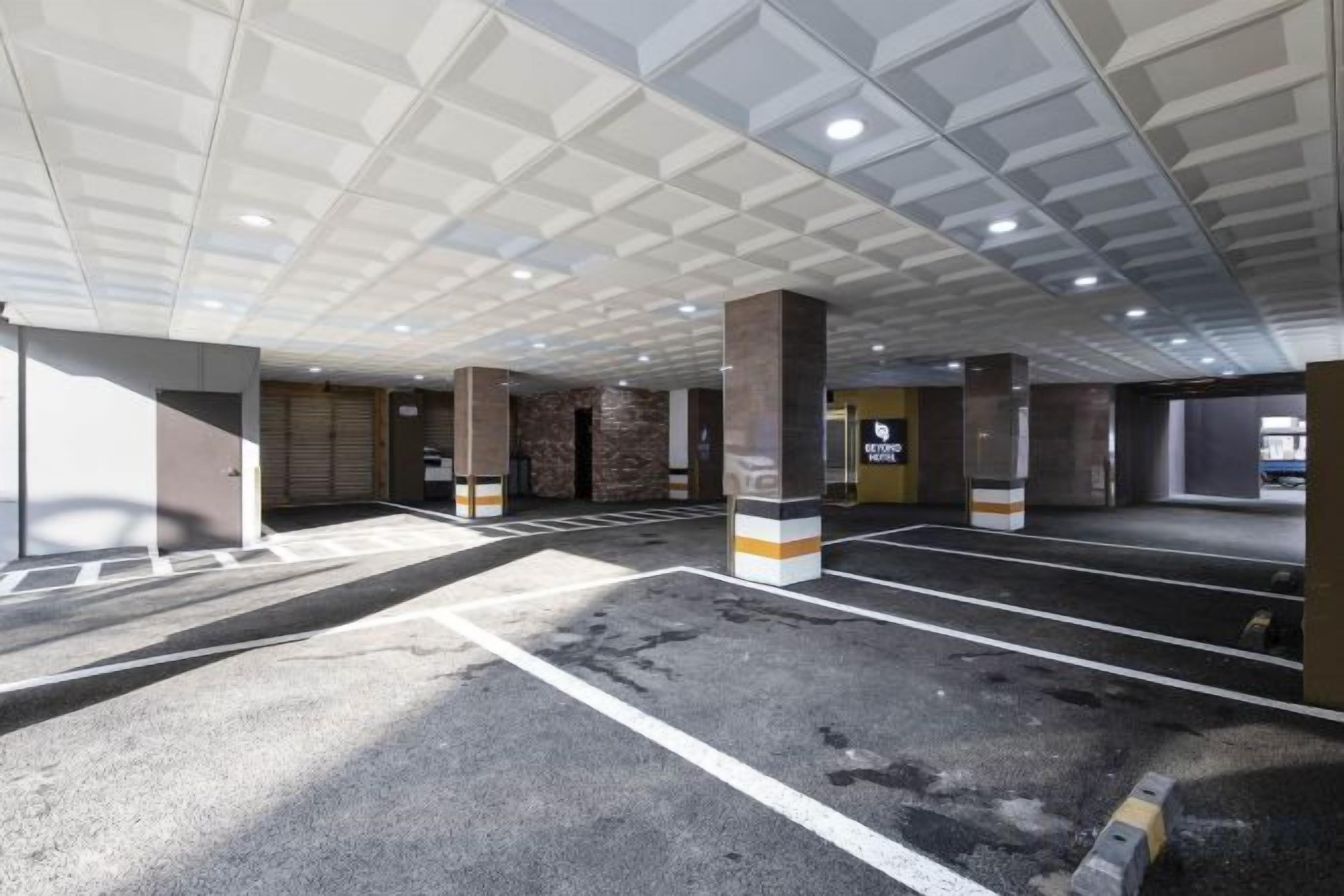 A parking garage with multiple parking spaces, concrete pillars, and a ceiling with recessed lighting.
