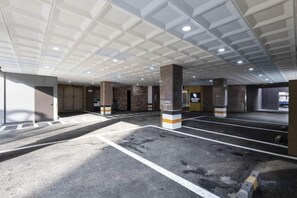 A parking garage with multiple parking spaces, concrete pillars, and a ceiling with recessed lighting. - Beyond Hotel (Incheon)