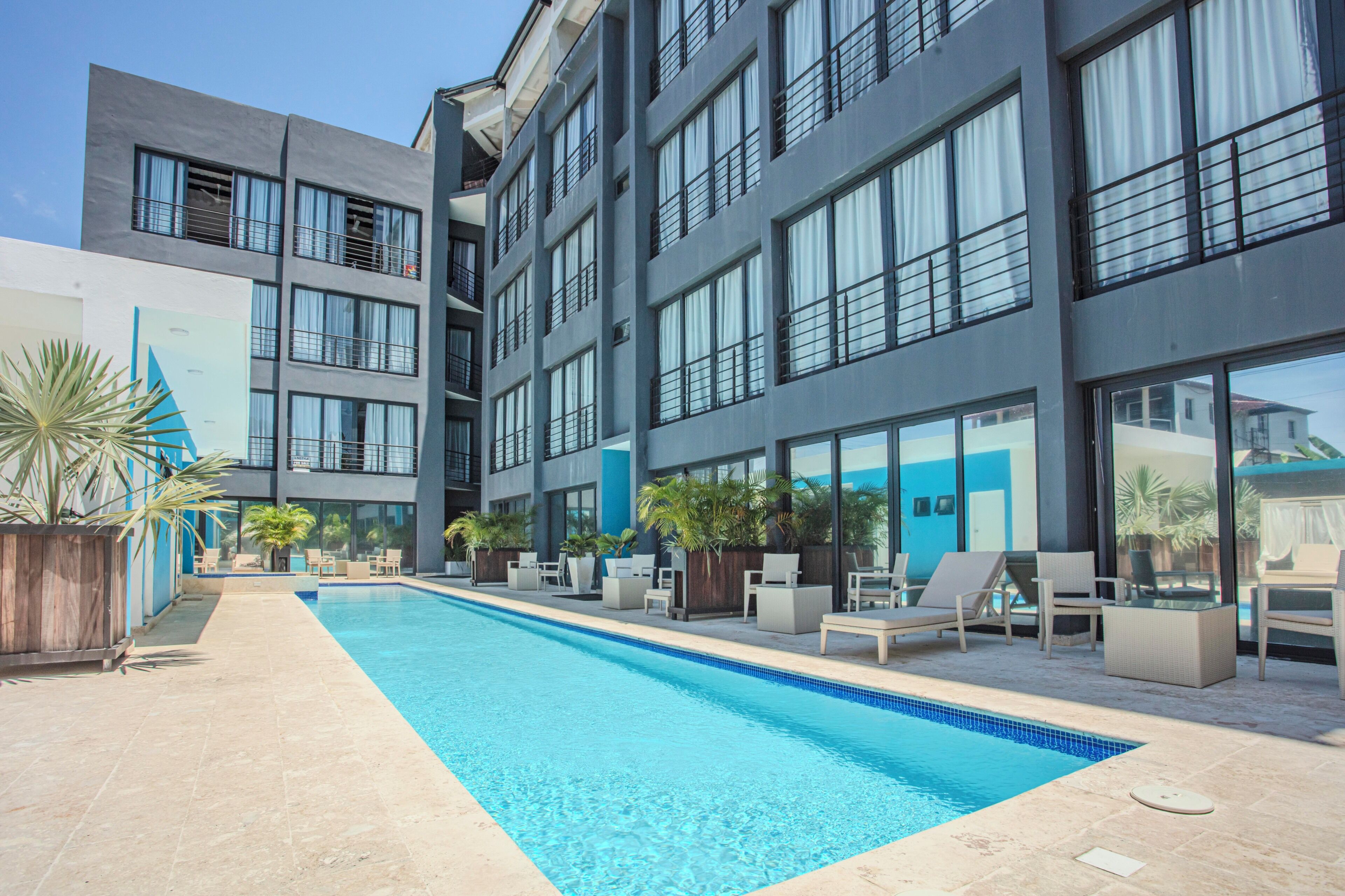 Et moderne hotel med pool, udendørs siddepladser og store vinduer.