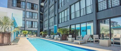 Et moderne hotel med pool, udendørs siddepladser og store vinduer.