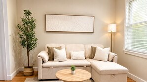 Una sala de estar con un sofá modular, una mesa de centro redonda, una planta en maceta y una obra de arte colgada en la pared.