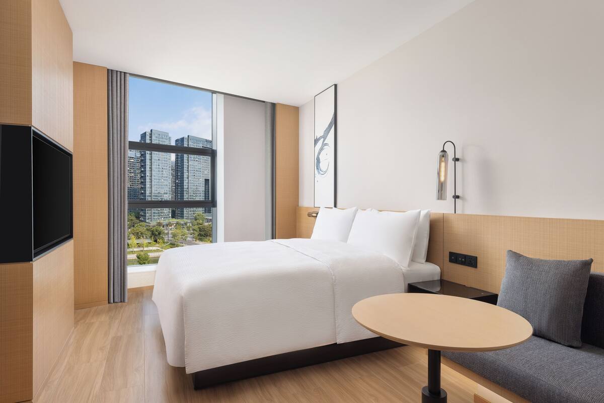 Une chambre d’hôtel moderne dotée d’un grand lit, d’un canapé, d’une petite table, d’une télévision et offrant une vue sur la ville.