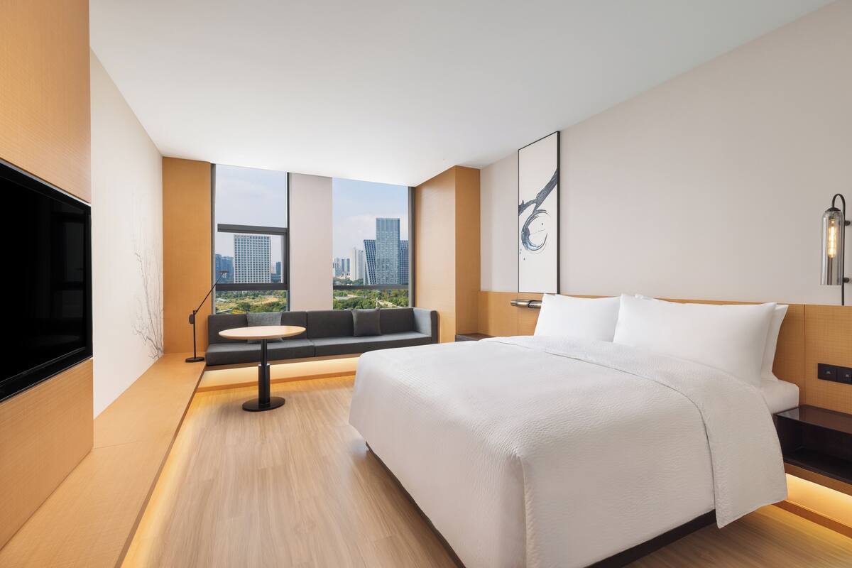 Une chambre d’hôtel moderne avec un grand lit, un canapé, une petite table ronde et un téléviseur.