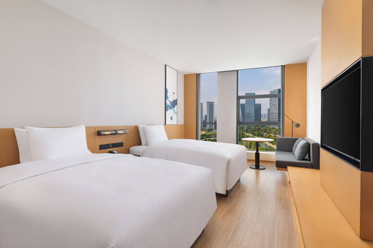 Une chambre d’hôtel moderne avec deux lits, un canapé, une télévision et une vue sur la ville.