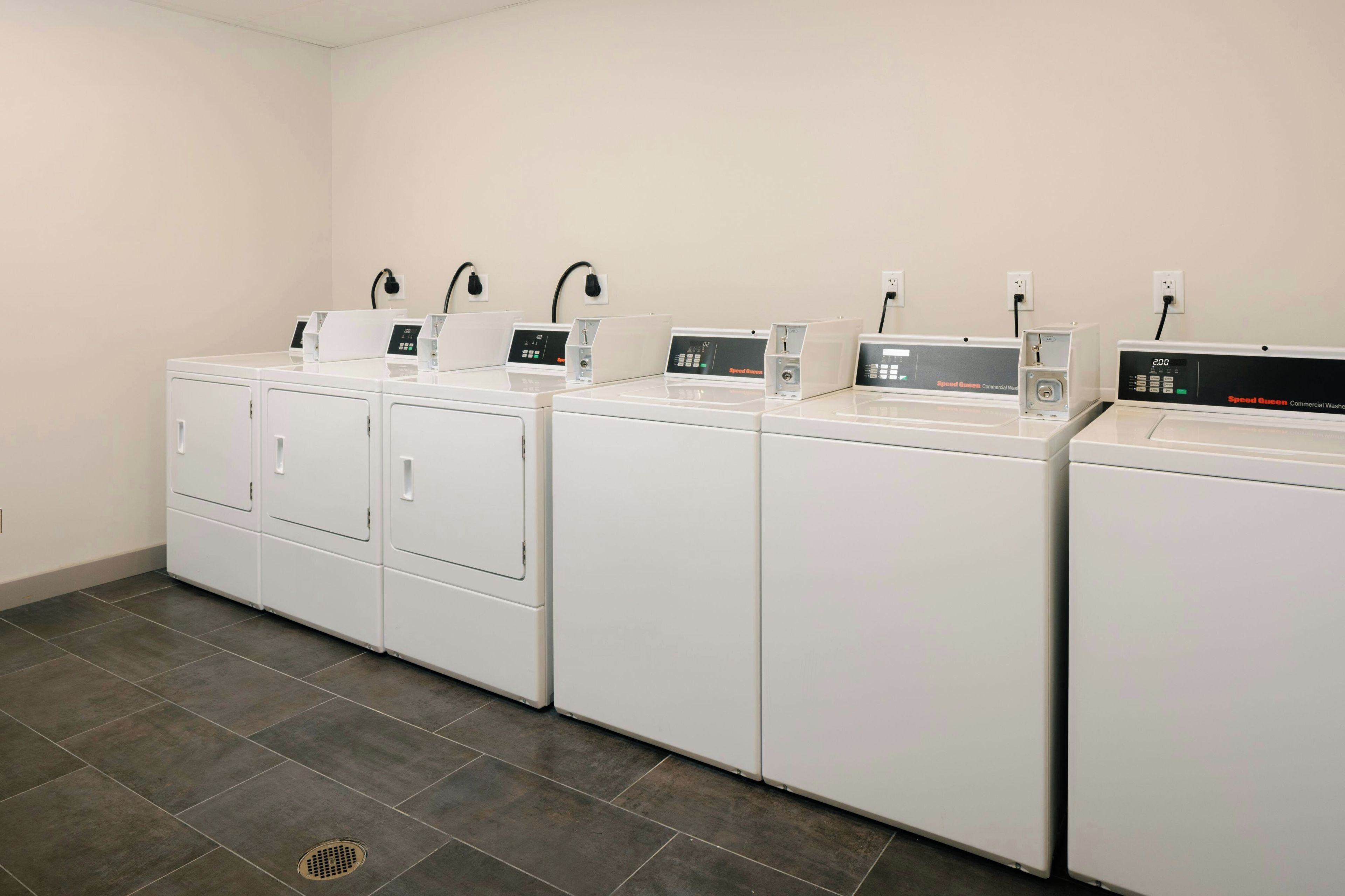 A laundry facility with four white washing machines and dryers, each with a digital control panel.