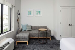 Ein modernes Zimmer mit einem anthrazitfarbenen Ecksofa, einem runden Holztisch, einer weißen Tür und zwei abstrakten Bildern an der Wand.