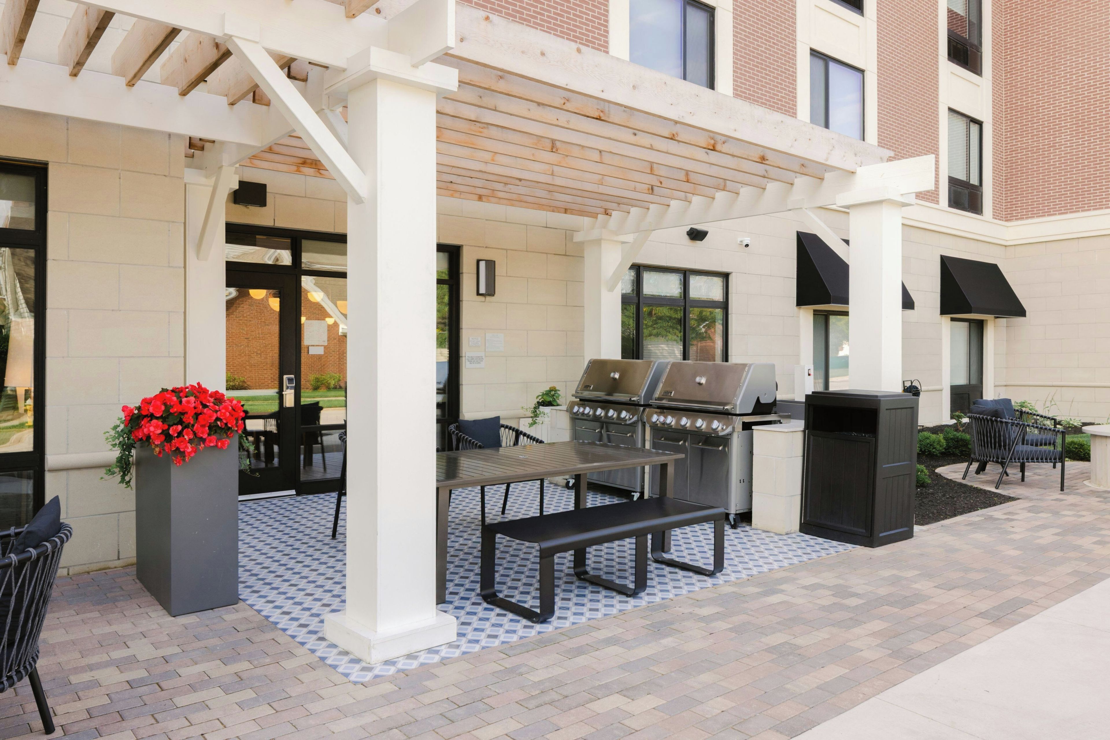 An outdoor patio with a grill, seating, and a planter with red flowers.