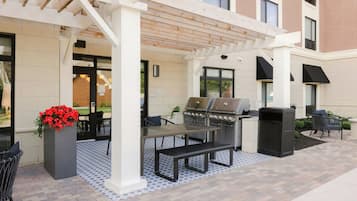 An outdoor patio with a grill, seating, and a planter with red flowers.