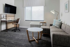 Ein modernes Wohnzimmer mit einem Flachbildfernseher, einem Schreibtisch, einem Sessel, einer Couch, einem runden Tisch und einer Stehlampe.