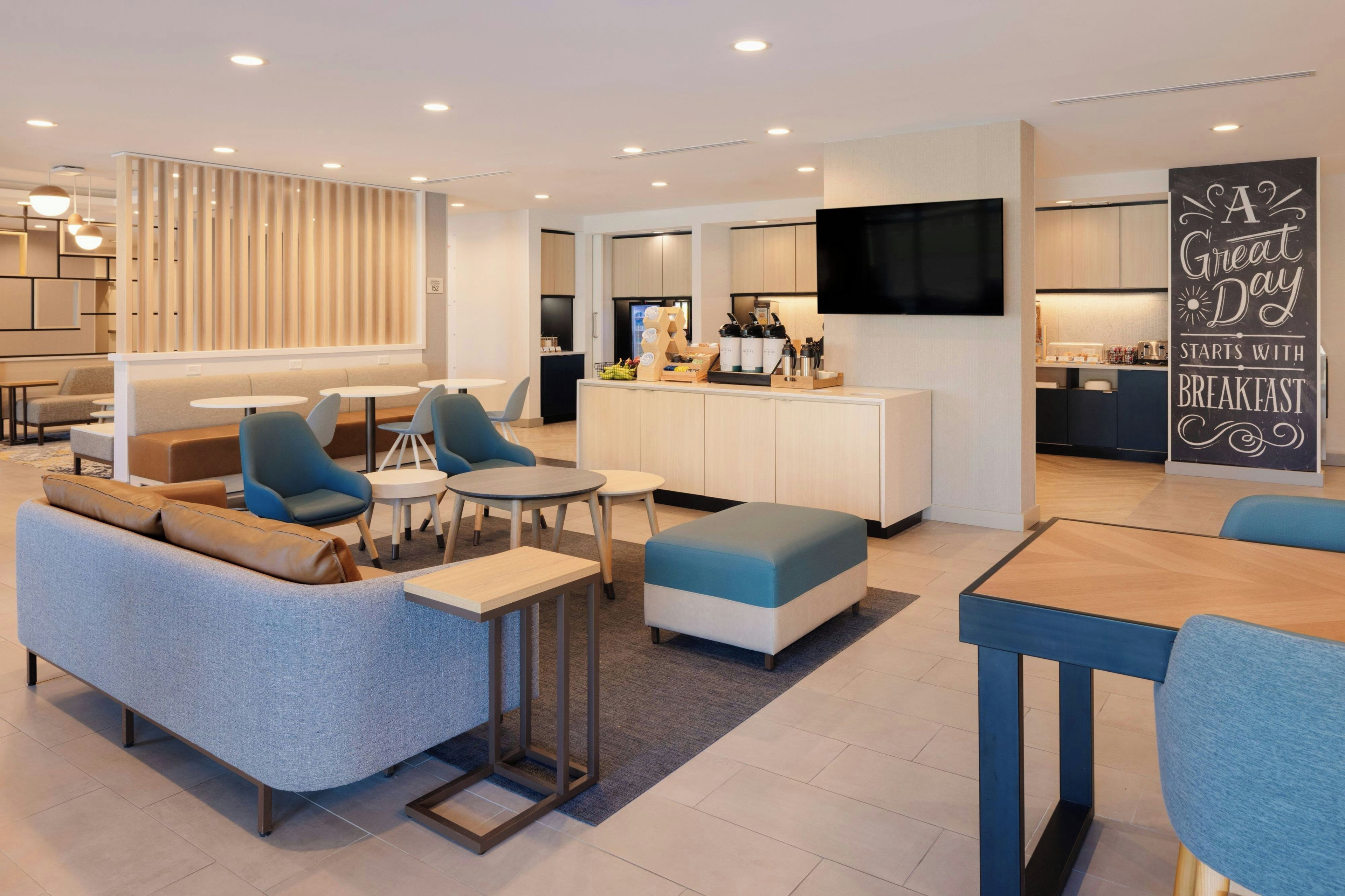 Una sala de estar moderna con sofá, sillas, una mesa de centro y una zona de cocina con televisor y mostrador.