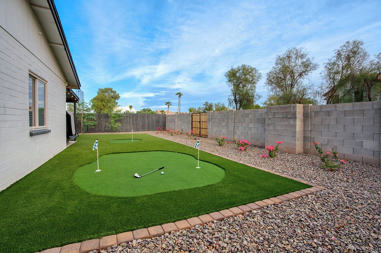 A backyard with a putting green, a brick wall, and a wooden gate.