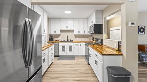 Una cocina moderna con armarios blancos, un refrigerador de acero inoxidable, encimeras de madera y un bote de basura negro.