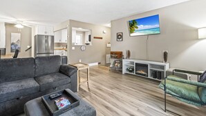 Un salón moderno con un sofá gris, una mesa de centro con revistas, un televisor de pantalla plana en la pared y piso de madera.