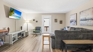 Una sala de estar con un sofá gris, una mesa de centro de madera, un televisor y una chimenea.