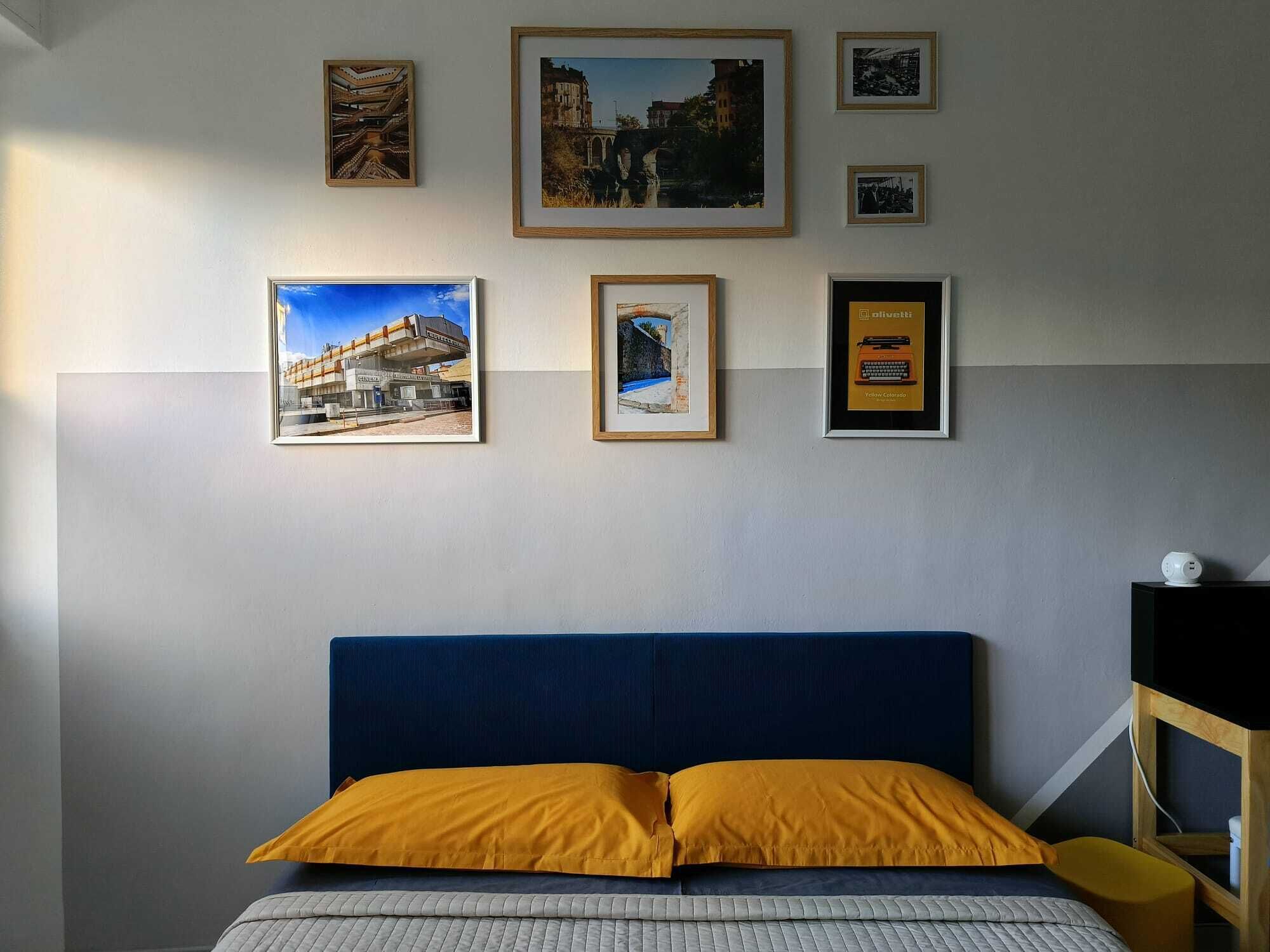 A bedroom with a blue headboard, a bed with a yellow pillow, and several framed pictures on the wall.