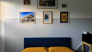 A bedroom with a blue headboard, a bed with a yellow pillow, and several framed pictures on the wall.