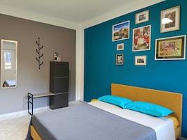 A bedroom with a bed, a wardrobe, a mirror, and a wall with framed pictures.