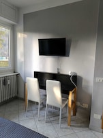 A room with a black TV mounted on the wall, a black desk with a white chair, and a radiator on the floor.