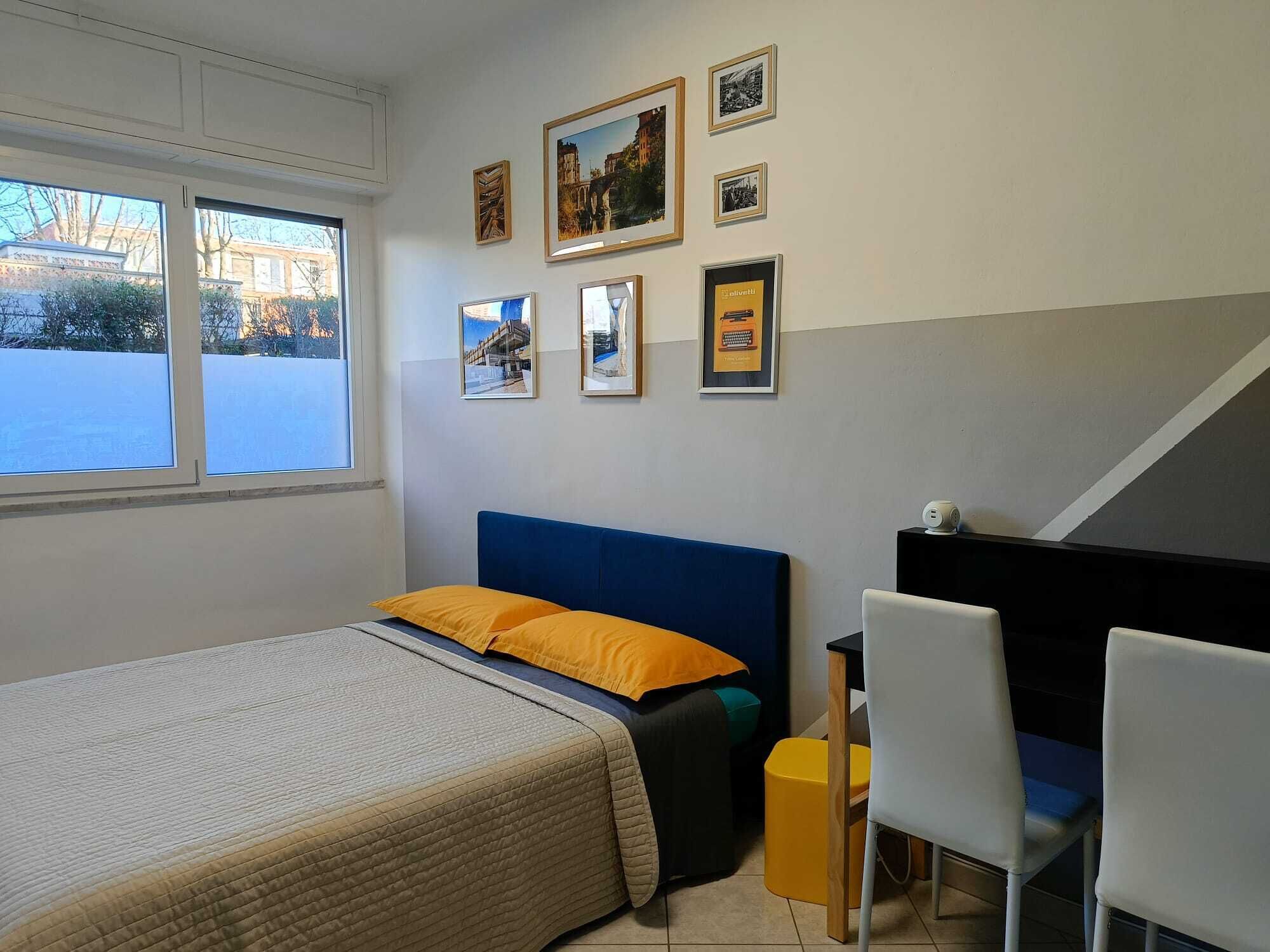 Une chambre à coucher avec un lit, un bureau et des chaises. Des tableaux encadrés ornent le mur.