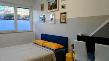 A bedroom with a bed, a desk, and chairs. There are framed pictures on the wall.