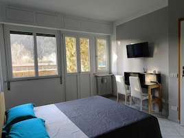 A bedroom with a bed, a desk, a chair, and a TV.