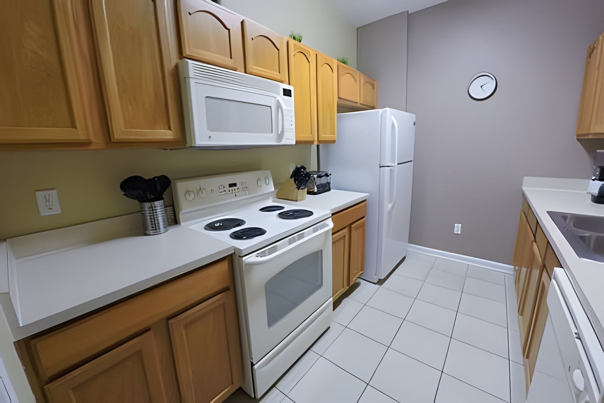 A kitchen with wooden cabinets, a white stove, a microwave, and a refrigerator.
