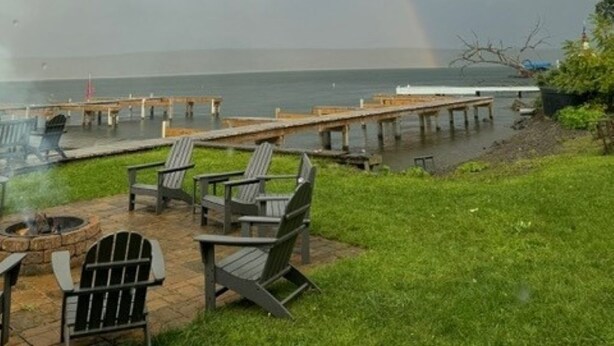 Un patio con sillas Adirondack y un brasero, con vista a un cuerpo de agua y un muelle.