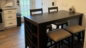 Un comedor con una mesa de madera oscura y dos sillas, una puerta blanca y una cocina con armarios blancos y un horno de acero inoxidable.